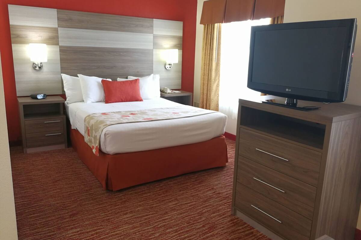 A hotel room with a bed, a TV, a nightstand, a drawer, and a cabinet.