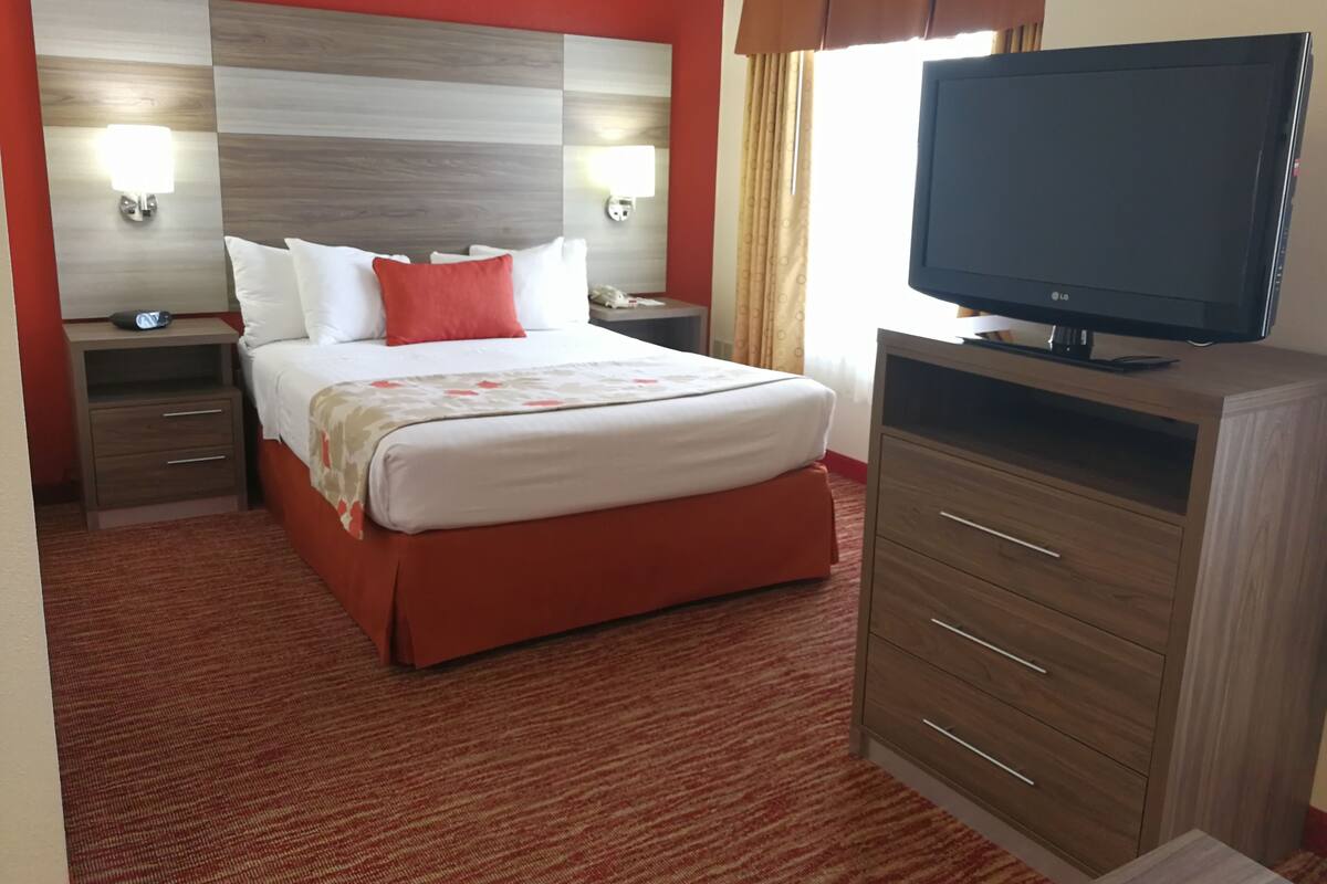A hotel room with a large bed, two bedside tables, a TV, and a wooden dresser.