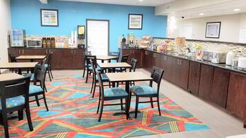 A restaurant with a blue wall, a counter with food items, and seating with chairs and tables.