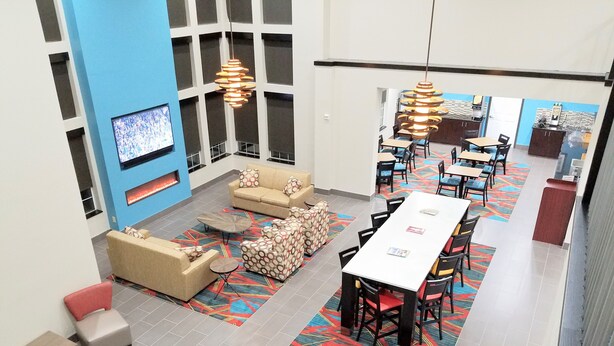 A spacious hotel lobby with a central seating area, a long dining table, and a TV mounted on the wall.