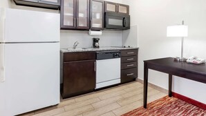 A compact kitchen with dark cabinets, a white refrigerator, a microwave, a coffee maker, and a small table with a lamp.