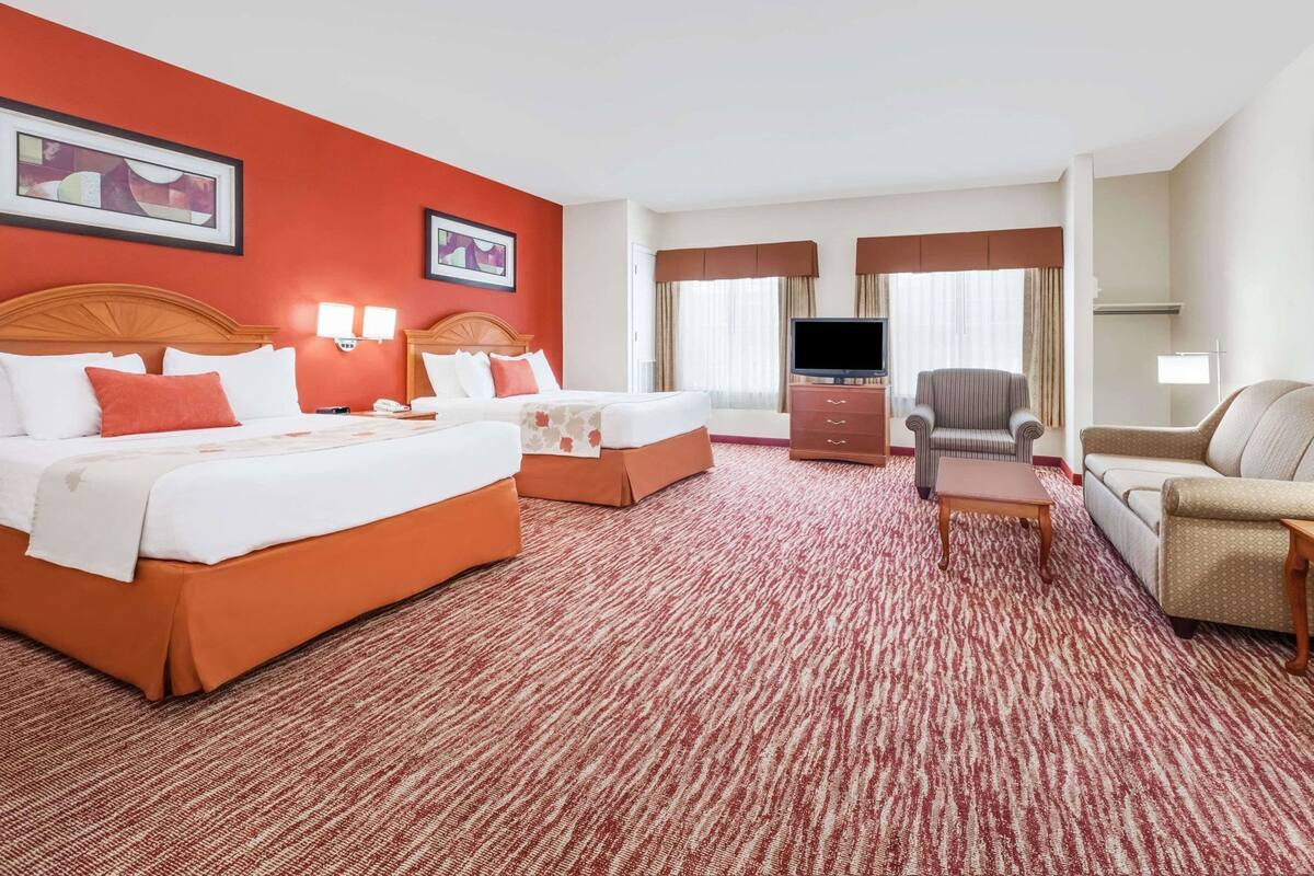 A hotel room with two beds, a TV, a sofa, and a desk.