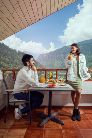 A terrace with a table set for two, overlooking a mountainous landscape.