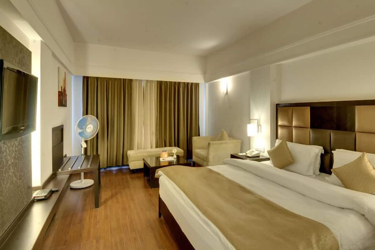 Una habitación de hotel con una cama grande, un escritorio, una silla, un televisor y un ventilador.