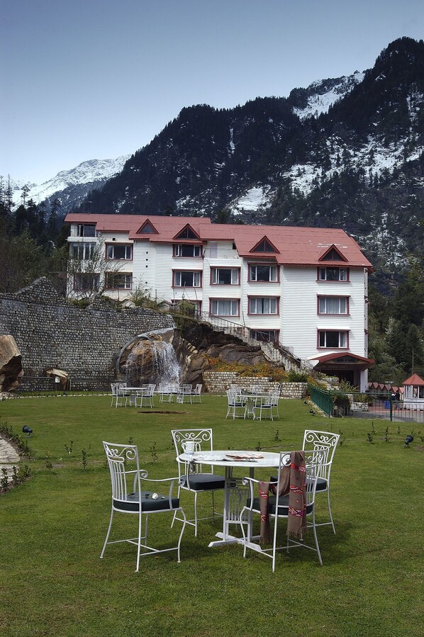 A hotel with a stone wall, a waterfall, and a mountain backdrop.