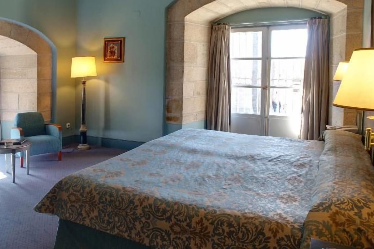 A hotel room with a large bed, two lamps, a chair, and a small table.