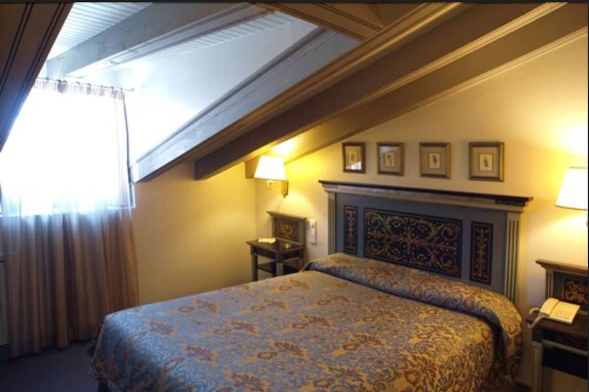 Une chambre d’hôtel avec un grand lit, une table de chevet, une lampe et un plafond doté d’une lucarne.