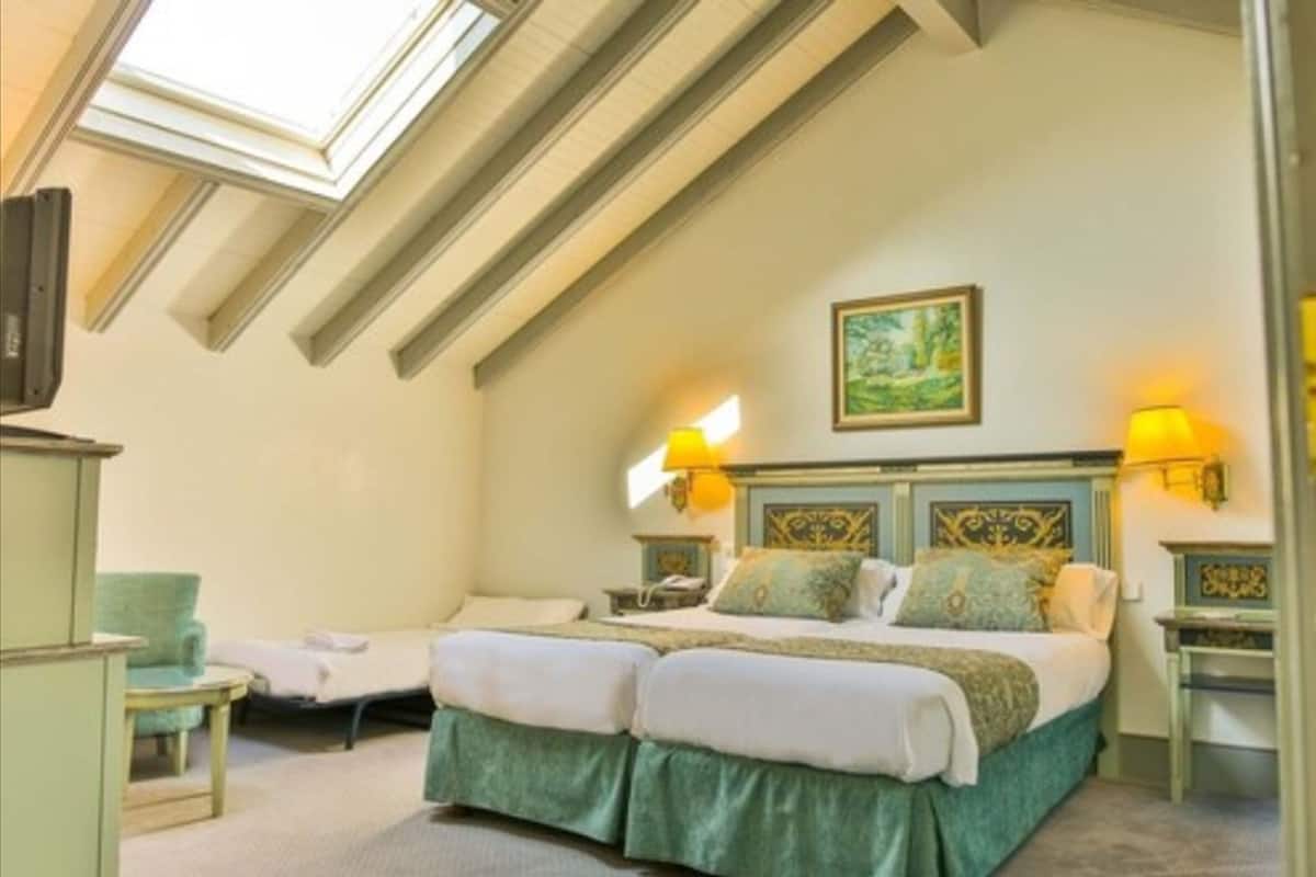 Une chambre avec un lit, deux tables de chevet, une chaise, un tableau au mur et une lucarne.