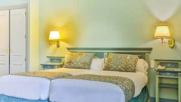 A double bed with floral-patterned pillows and a matching headboard, two bedside lamps, and a green nightstand with a telephone.