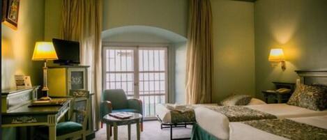 Habitación de hotel con cama, escritorio con lámpara, silla y ventana con cortinas.
