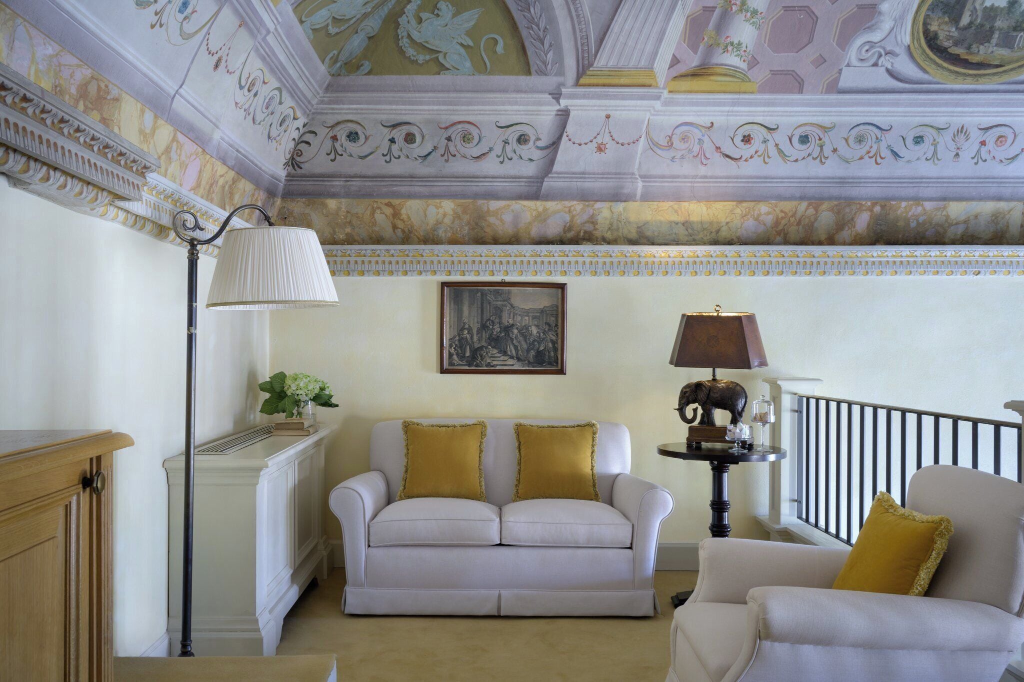 A room with a white sofa, a table with a lamp, and a painting on the wall.