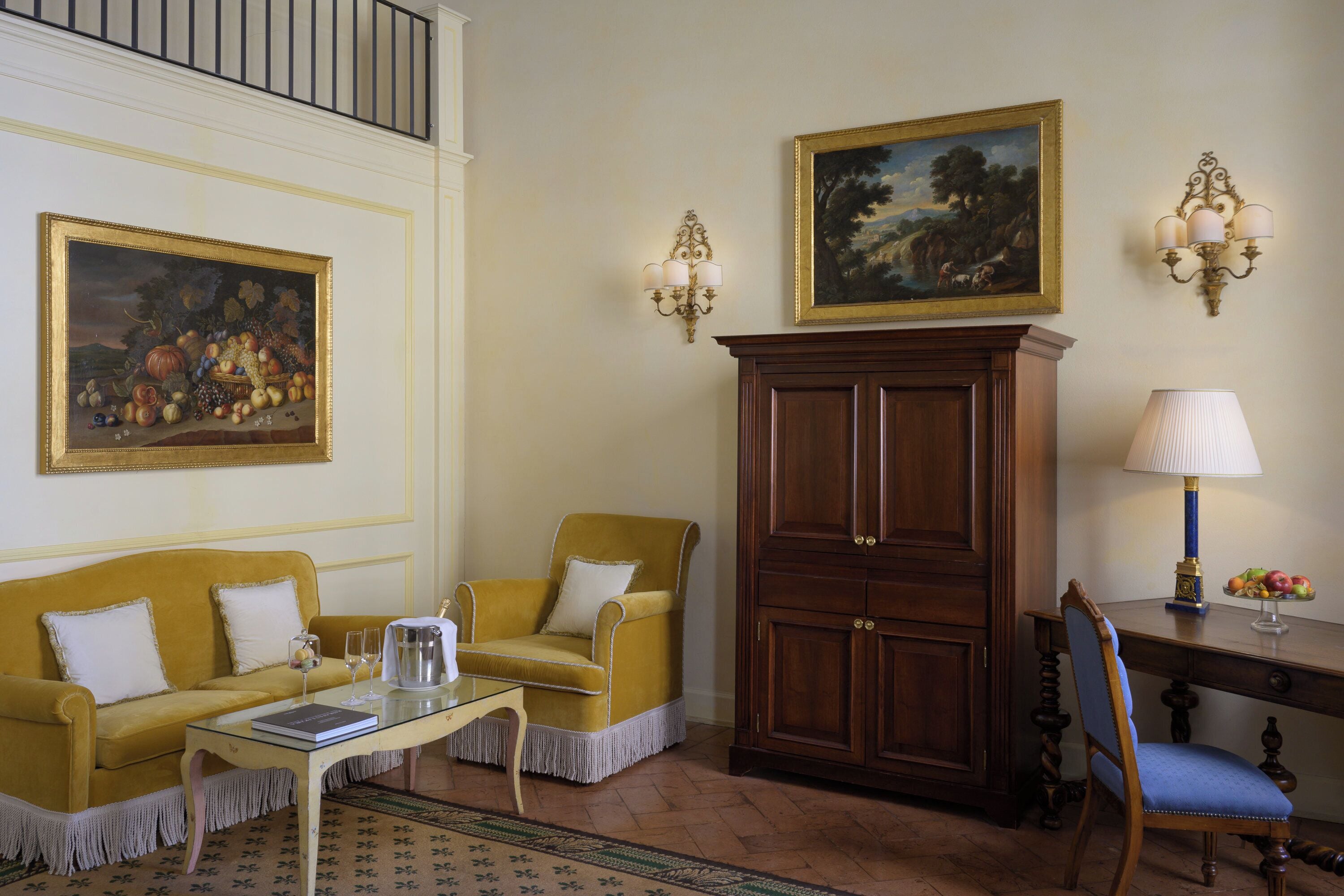 Une pièce avec un canapé jaune, un meuble en bois, un bureau avec une lampe et deux appliques murales.