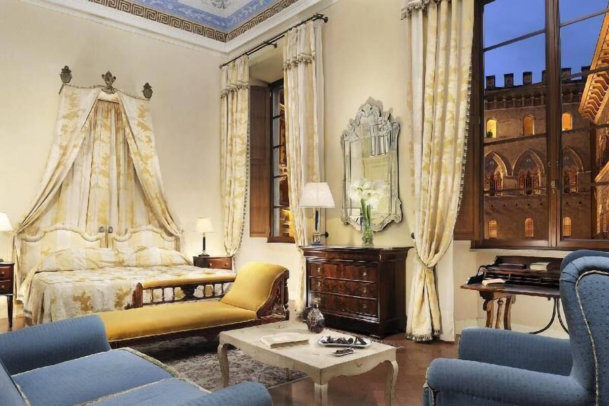 A bedroom with a four-poster bed, a sofa, a coffee table, a dresser, and a mirror.