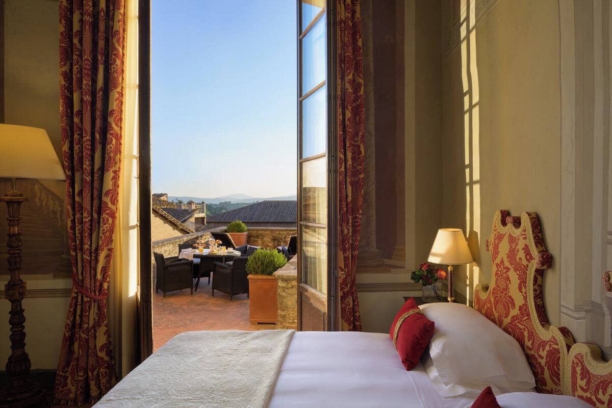 A hotel room with a bed, a view of the cityscape, a dining area with a table and chairs, and a window with curtains.