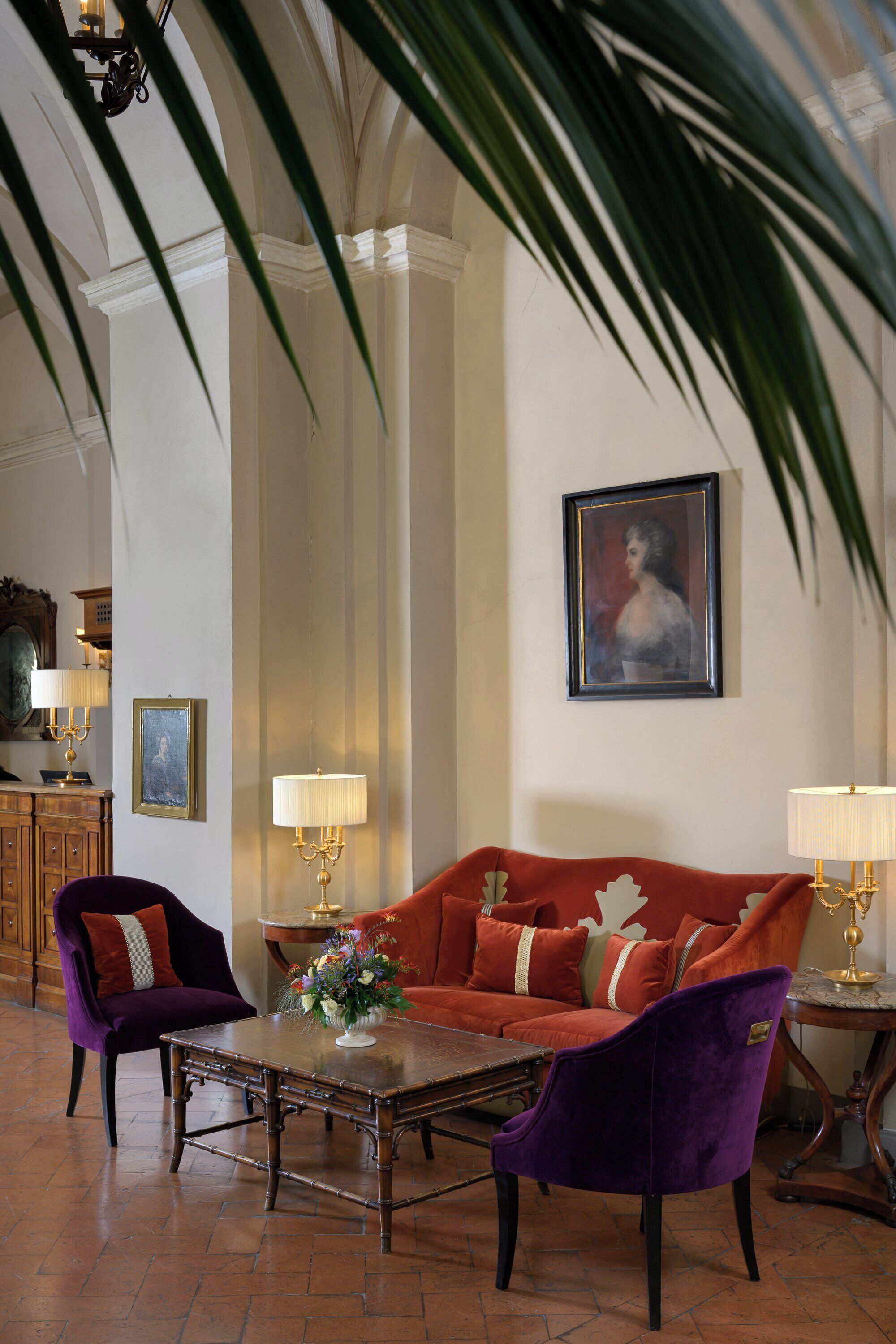A room with a red sofa, two purple chairs, a wooden coffee table, and a painting on the wall.