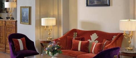 A room with a red sofa, two purple chairs, a wooden coffee table, and a painting on the wall.