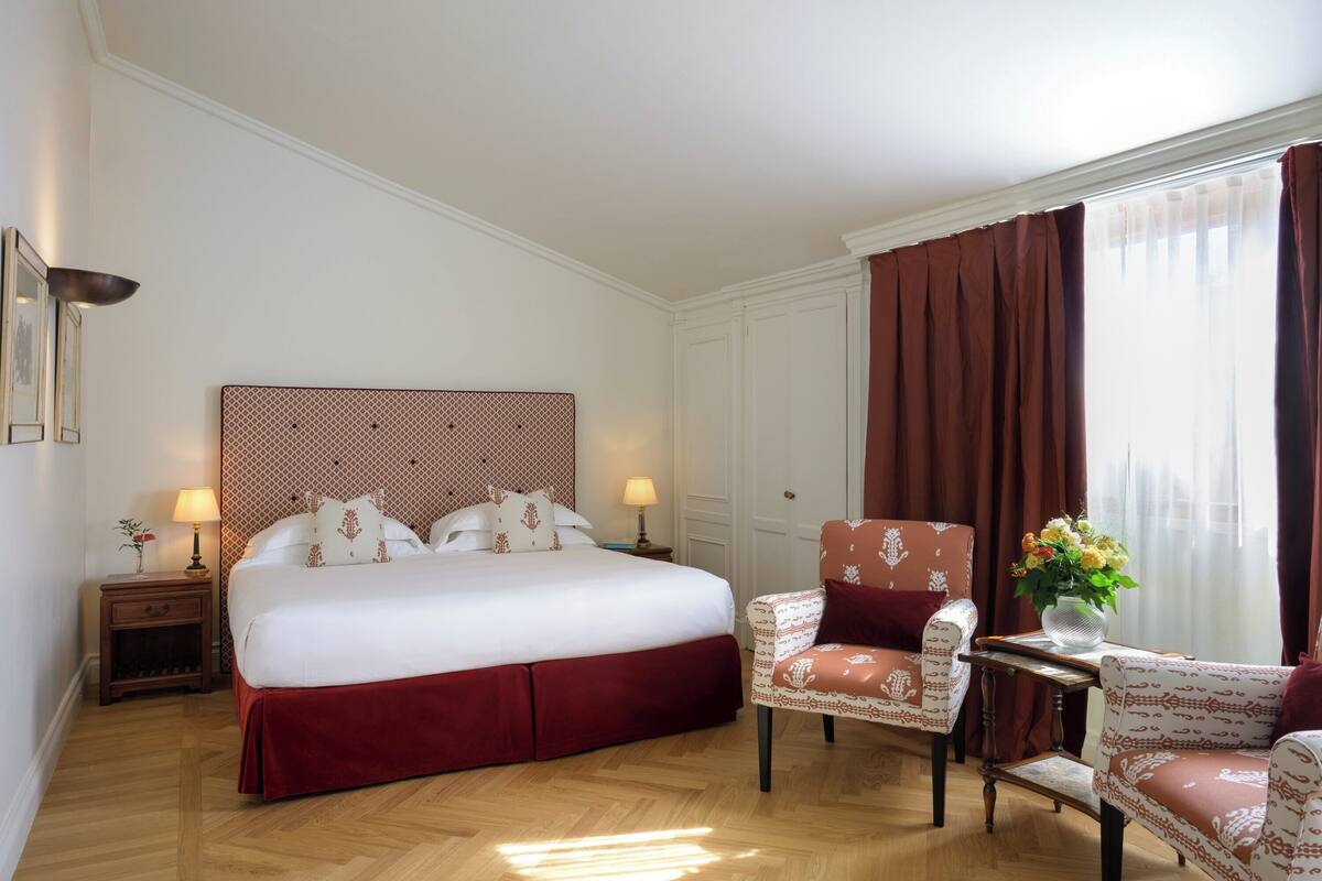 A hotel room with a large bed, two bedside tables with lamps, a chair, and a window with curtains.