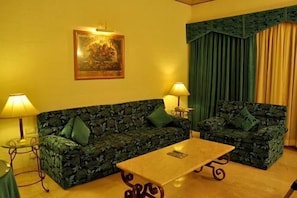 A living room with two green patterned sofas, a wooden coffee table, lamps, and a framed picture on the wall. - Golden Palms Hotel And Spa (Bengaluru)