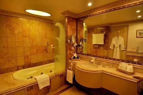 A spacious bathroom with a large bathtub, a separate shower area, a vanity with a mirror, and a robe hanging on the wall. - Golden Palms Hotel And Spa (Bengaluru)