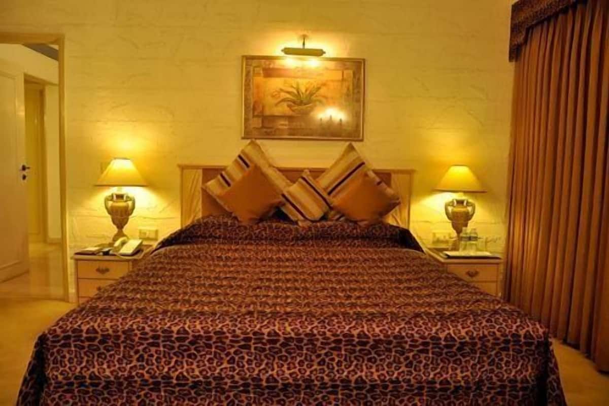 A hotel room with a large bed, two bedside tables with lamps, a painting above the bed, and a door to the left.
