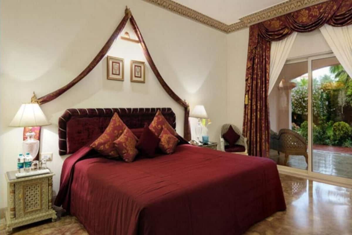 A bedroom with a large bed, a nightstand, a lamp, and a view of the outdoors.
