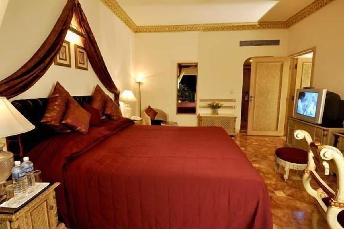 A hotel room with a large bed, a television, and a desk with a lamp.