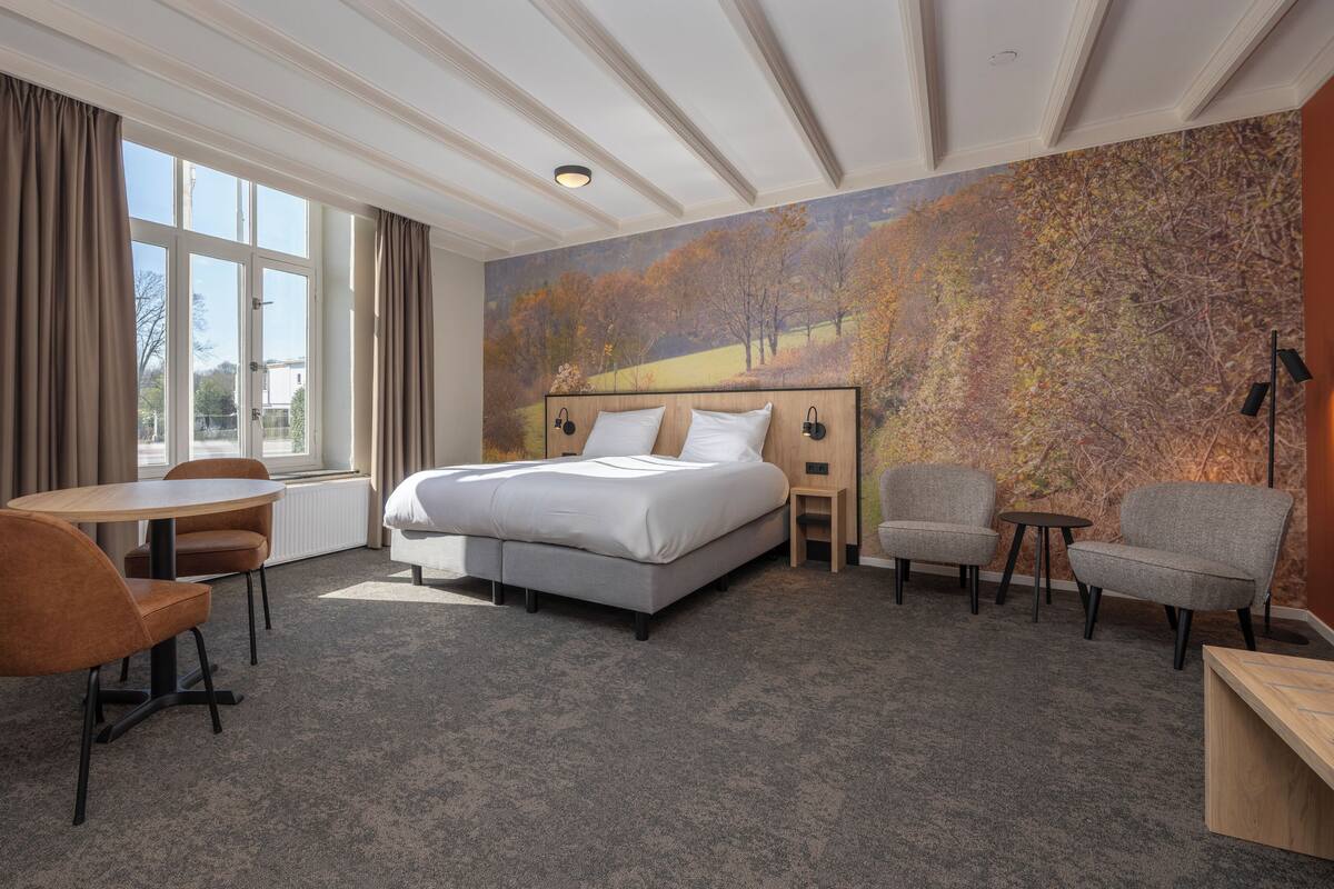 Habitación de hotel con una cama grande, un escritorio, dos sillas y vistas a árboles por la ventana.