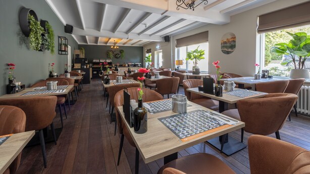 Un restaurante con mesas de madera y sillas marrones, una araña y plantas en macetas.