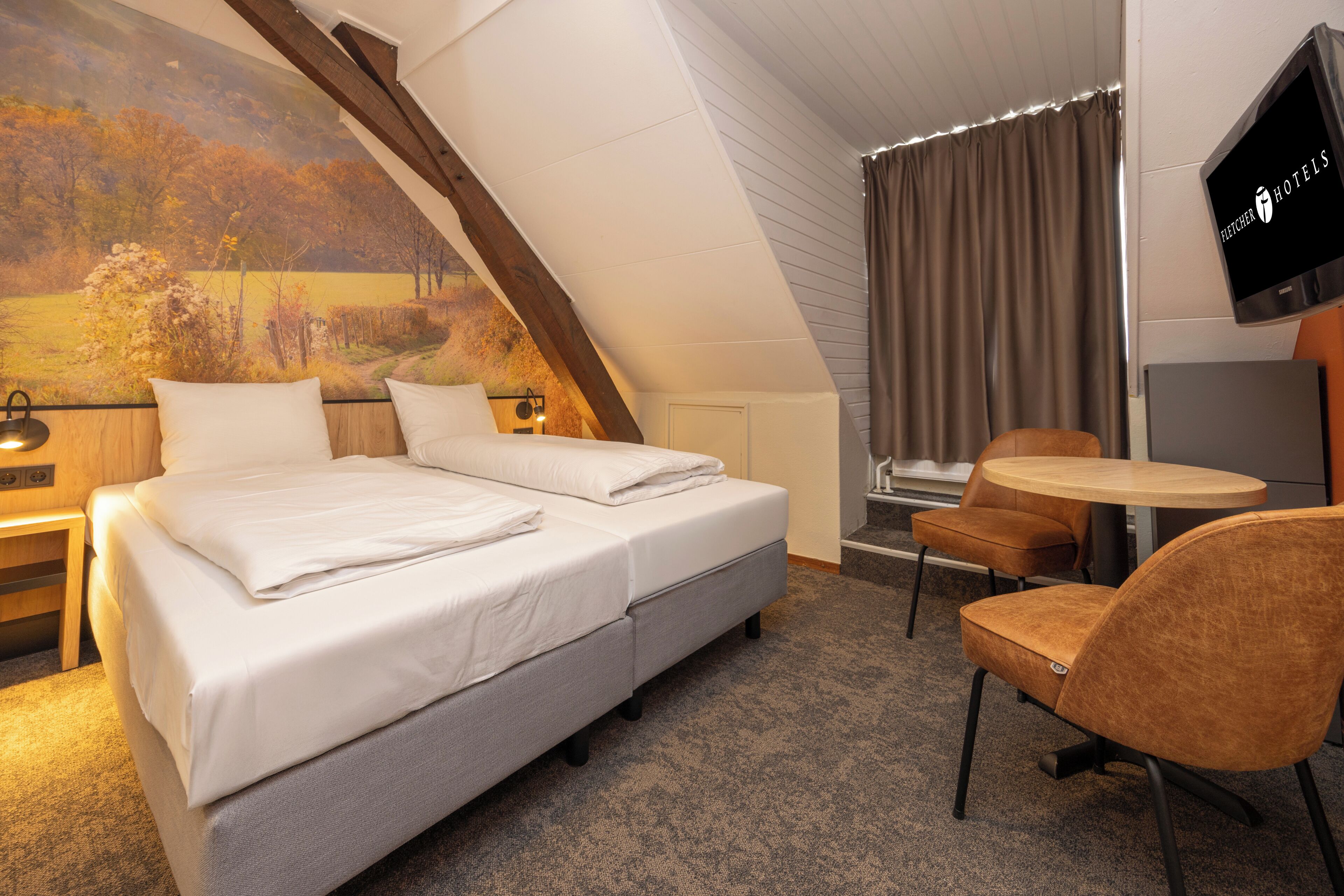 A hotel room with a bed, two chairs, a small table, a TV, and a painting on the wall.