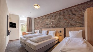 Habitación de hotel con dos camas, una pared de ladrillo, un televisor y un ventanal con cortinas.