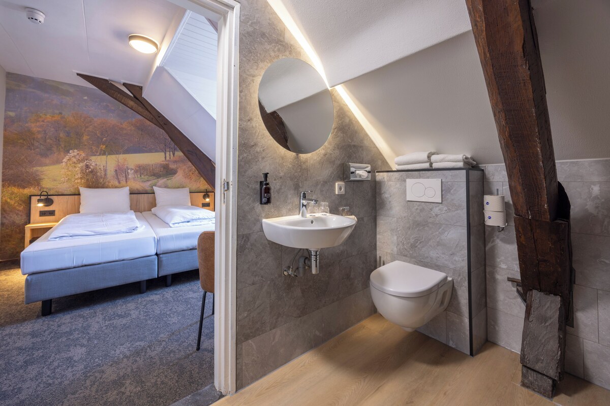 A bedroom with a bed, a bathroom with a sink and toilet, and a view of a landscape through a window.