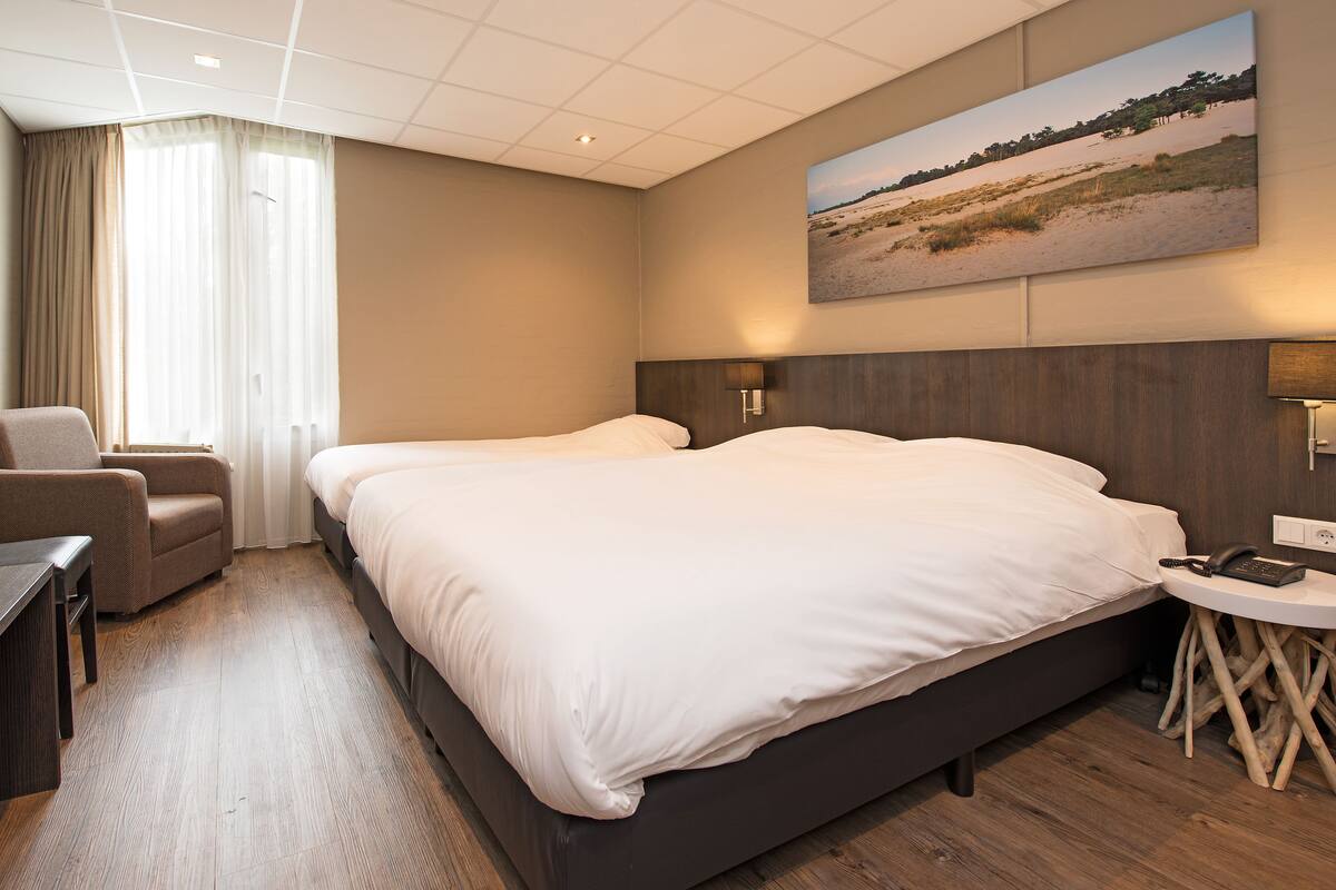 A hotel room with a large bed, a chair, a desk, and a painting of a beach scene.