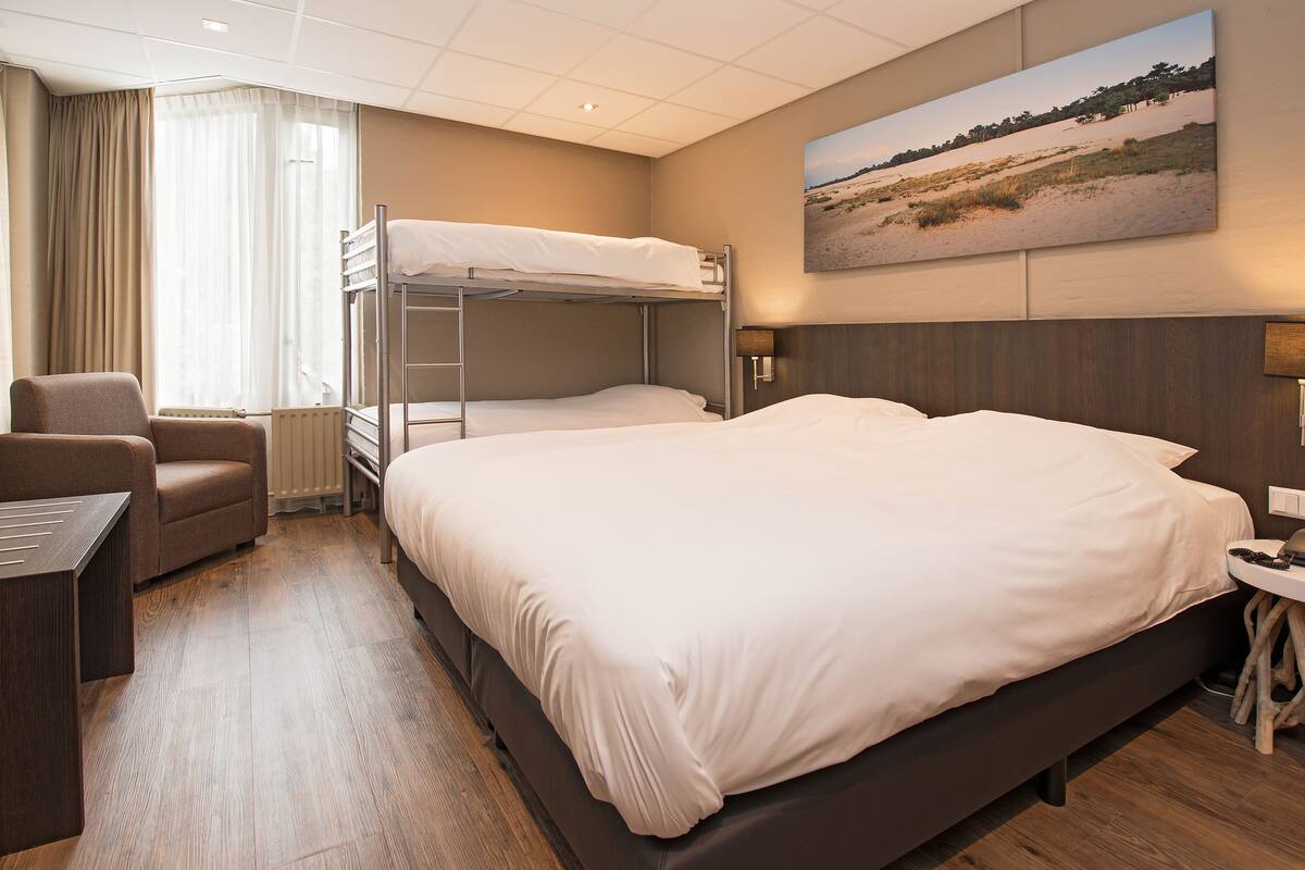 A hotel room with a large bed, a smaller bunk bed, a desk, and a chair.