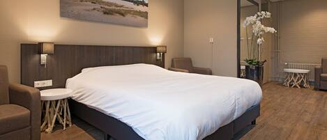 A modern hotel room with a large bed, a small round table, a chair, and a potted orchid.