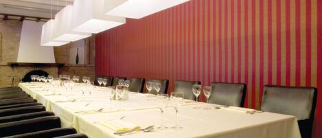 A long dining table set with chairs, white tablecloths, and wine glasses.
