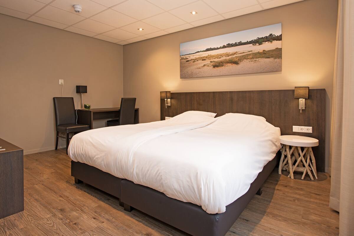 A modern hotel room with a large bed, a desk, and a chair.