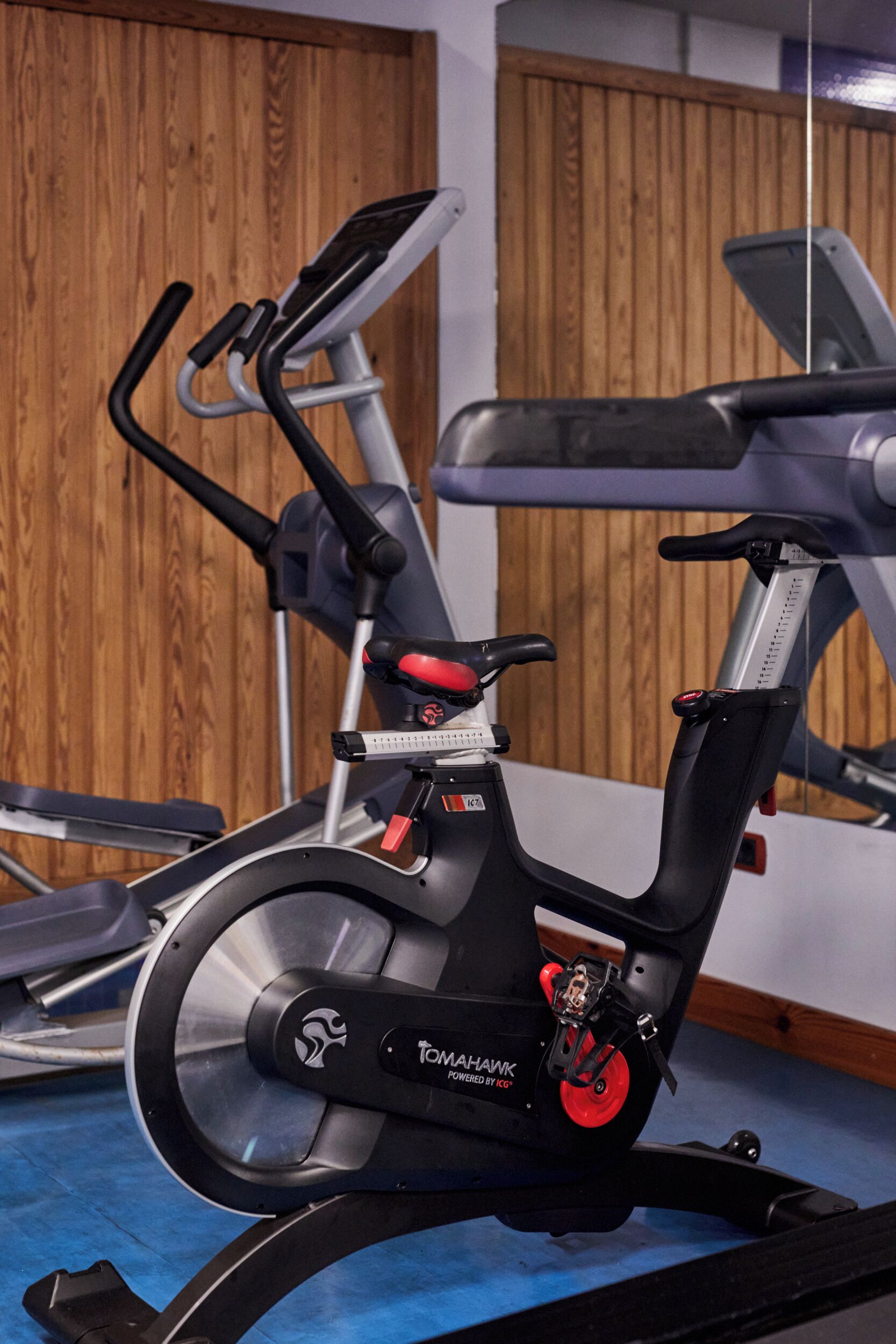 Ein stehendes Fahrrad mit digitalem Display, roten Pedalen und einem markenbezogenen Logo.