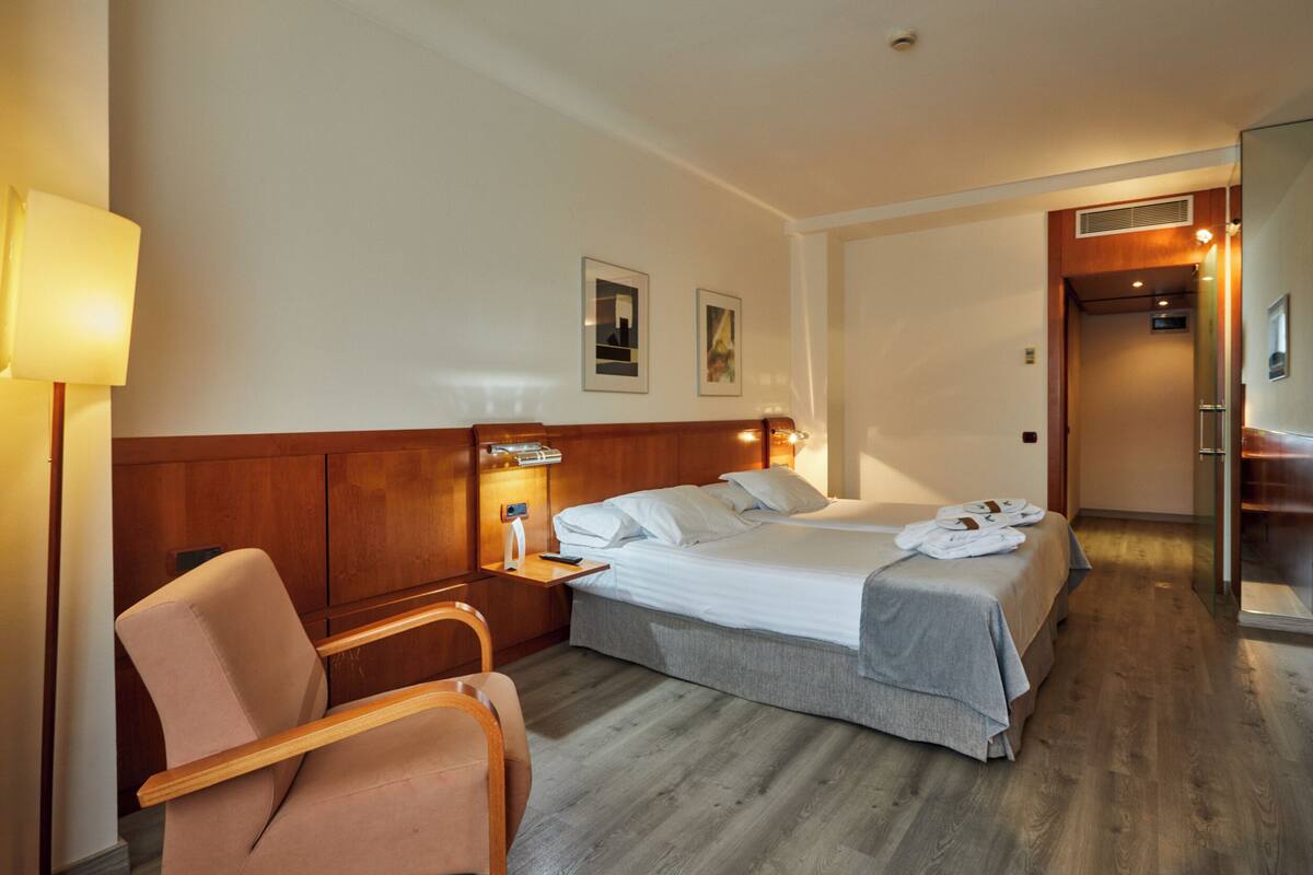 Une chambre d’hôtel avec un lit, une chaise, une table de chevet et une lampe.