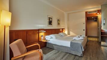 A hotel room with a bed, a chair, a nightstand, and a lamp.