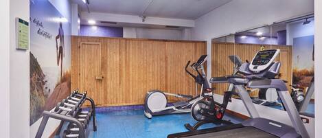 Une salle de sport équipée de matériel d’exercice, avec des murs recouverts de panneaux en bois et un sol bleu.