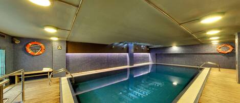 Una piscina interior con solárium de madera, flotadores salvavidas y pared de azulejos.