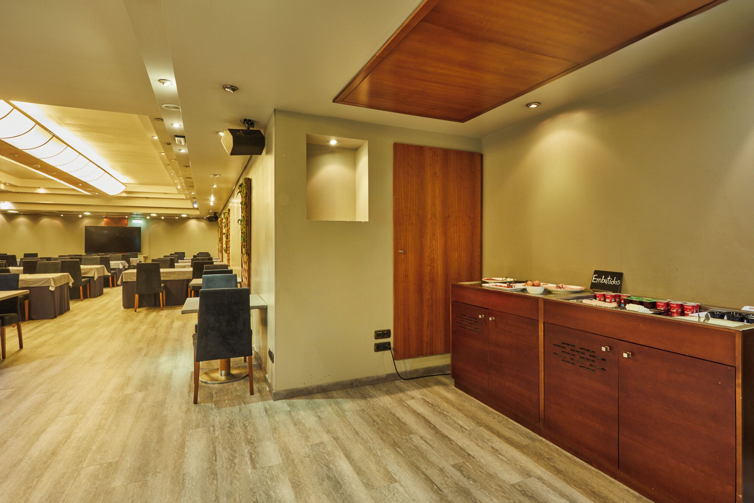 A conference room with tables and chairs, a wooden cabinet with food items, and a television on the wall.