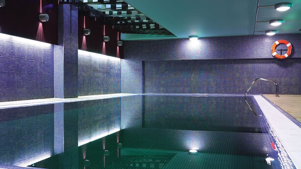 Una piscina interior moderna con una pared de pantalla digital y un flotador en la pared.