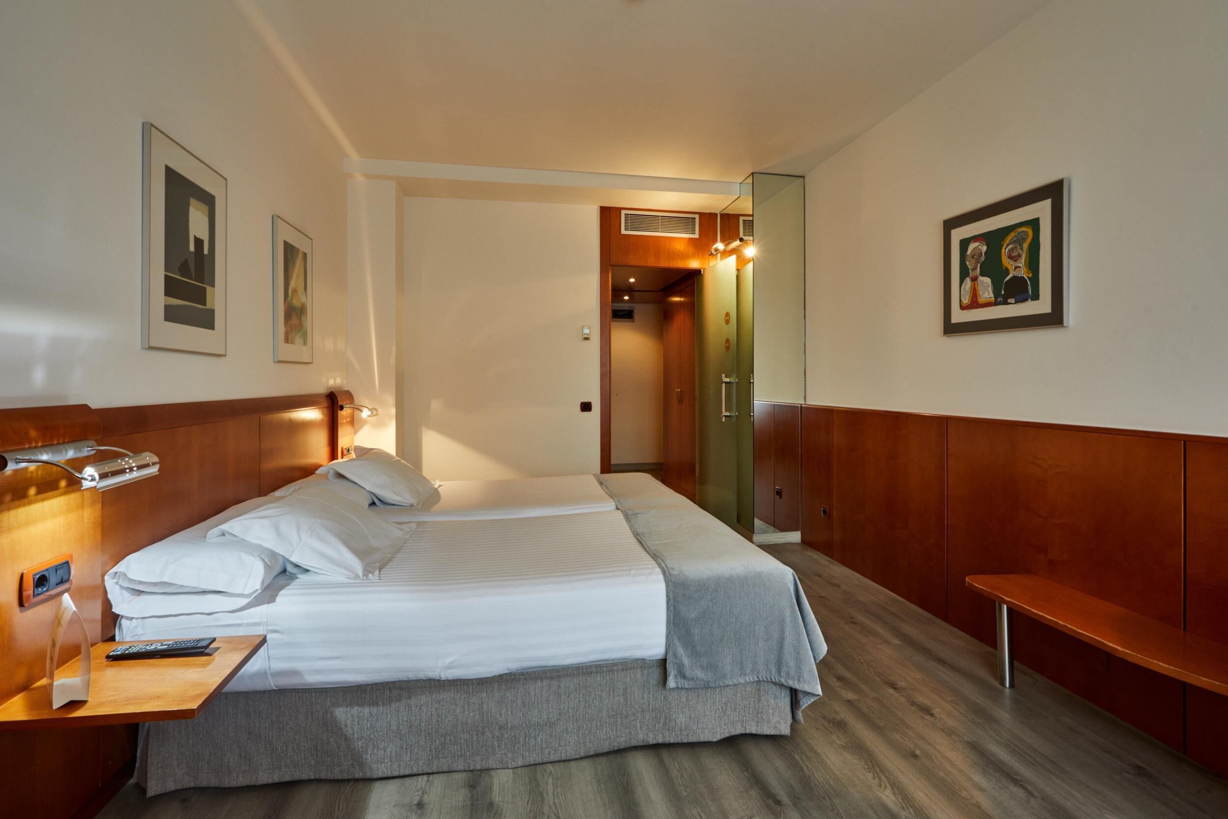 Una habitación de hotel con cama, mesita de noche y un banco.