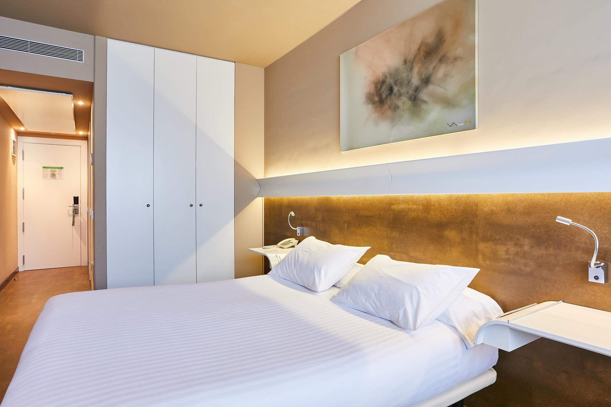 Una camera d'albergo con un letto grande, un comodino con una lampada, un telefono a muro e un quadro sopra il letto.