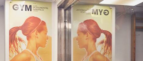 Un gimnasio con un espejo grande, un banco de madera con toallas y un cartel de una mujer ejercitándose.