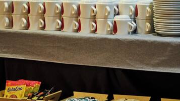 A table with stacked white mugs and plates, and wooden boxes containing snacks.
