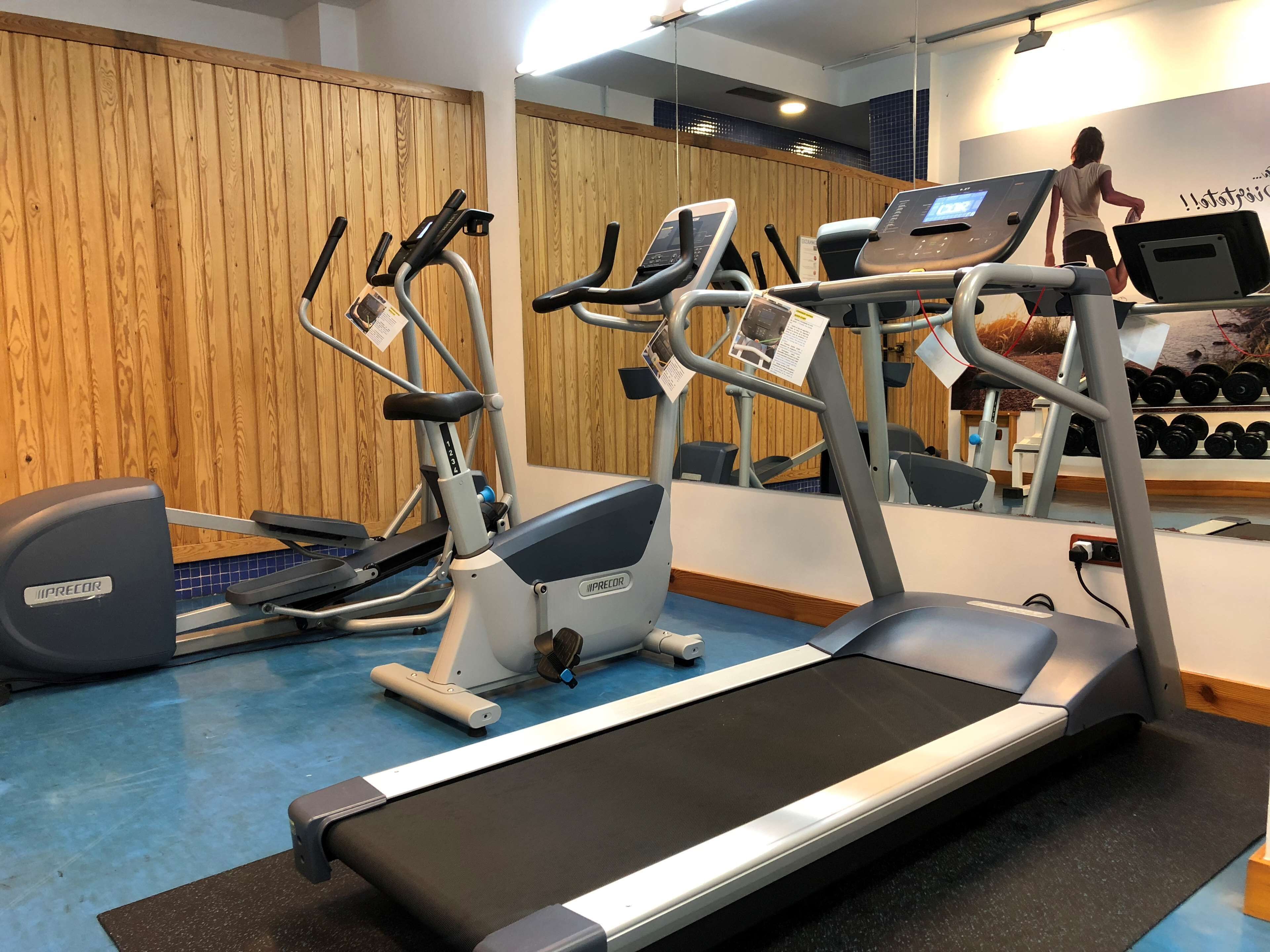 Un gimnasio con cintas de correr, elípticas y un espejo grande.