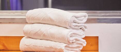 A stack of white towels on a wooden shelf in a bathroom.
