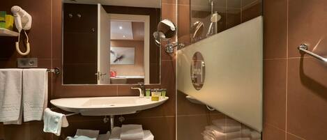 Un baño moderno con ducha envuelta en vidrio, un lavabo con espejo y un secador de pelo montado en la pared.